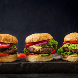 Three hamburger with beef meat burger and fresh vegetables on dark background. Tasty food.